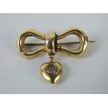 A yellow metal brooch in the form of a bow having heart suspended below, 2.8cm wide, 2.