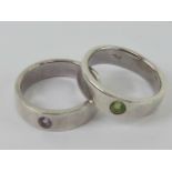 A pair of rings each stamped 925, one with lime green stone, the other with purple stone,