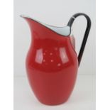 A red and black enamelled tin water jug standing 26cm high.