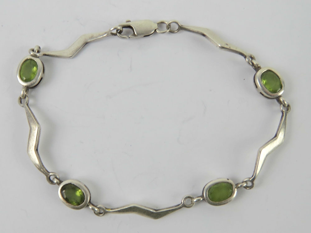 A silver and peridot bracelet having four oval cut stones separated by lightning bolt shaped panels,