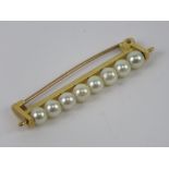 A yellow metal brooch set with eight pearls on wire bar, no apparent hallmarks, 4cm in length, 3.4g.
