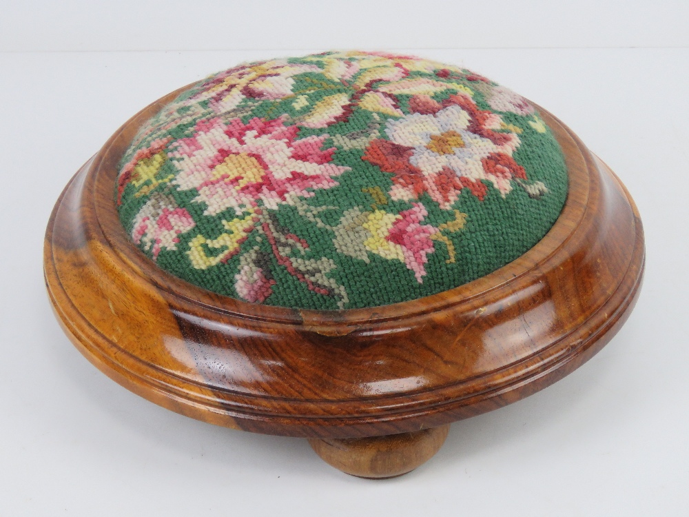 A contemporary circular needlepoint footstool in yew wood raised over three bun feet, 28cm wide.