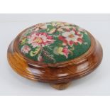 A contemporary circular needlepoint footstool in yew wood raised over three bun feet, 28cm wide.