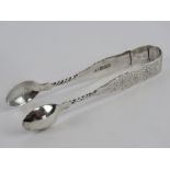 An HM silver pair of sugar tongs having floral engraving upon and hallmarked Birmingham 1892 with