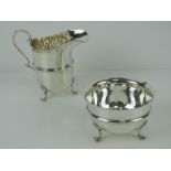 An HM silver sugar bowl and cream jug each raised over three clam shell legs,