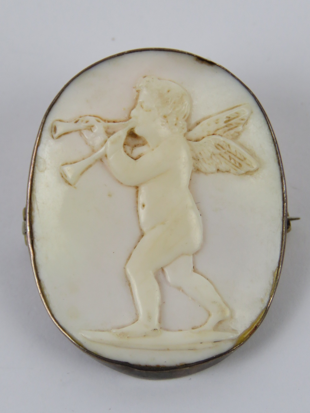An 'angel skin' coral carved cameo in the form of a cherub playing a musical instrument,