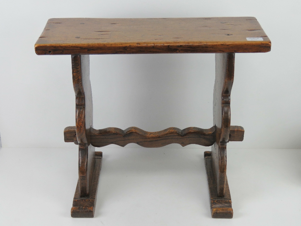 An early 20th century joint stool in oak, plank top and supports united by shaped trestle stretcher,