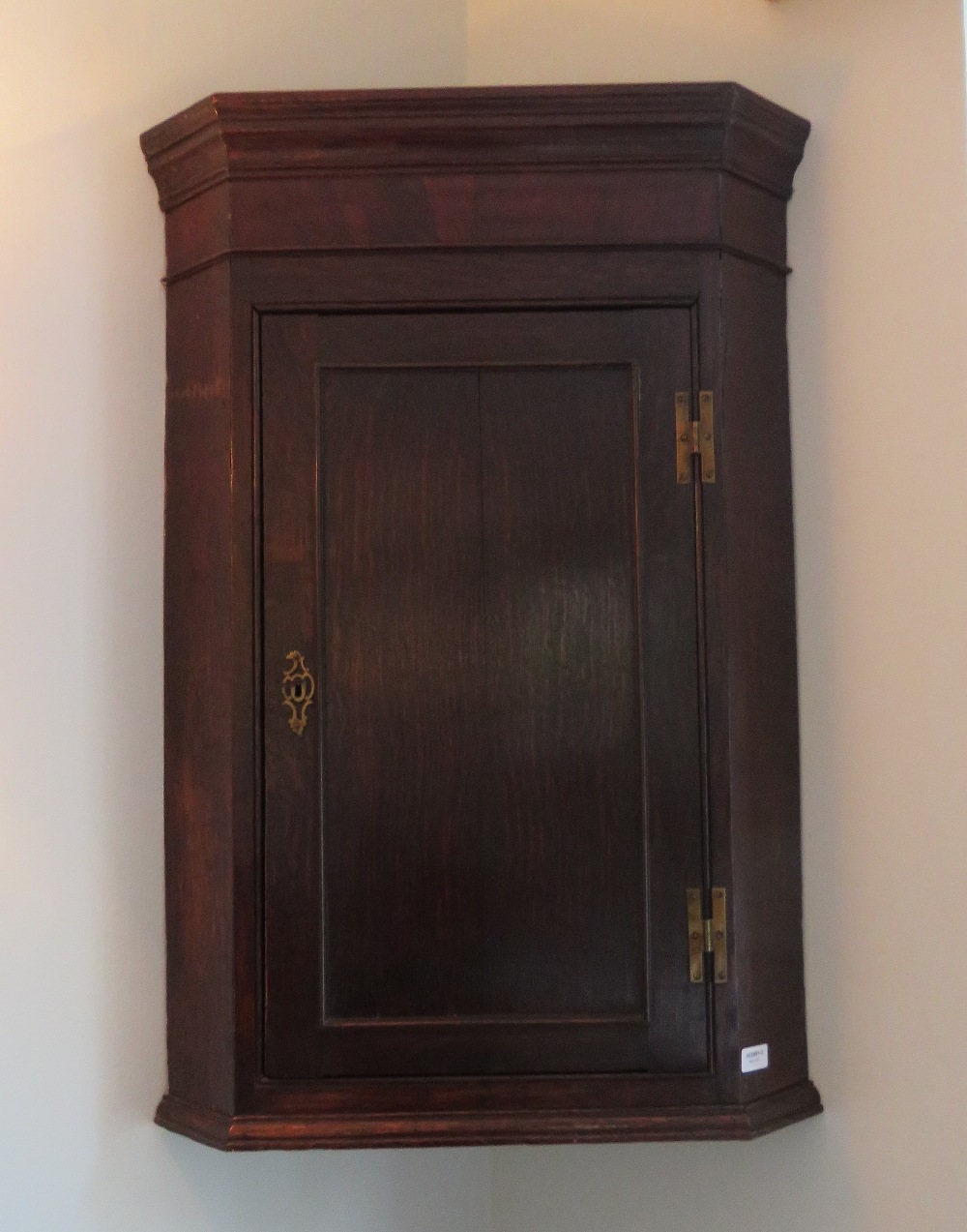 A Georgian oak hanging corner cabinet, door opening to reveal straight cut shelves within,