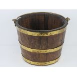 A coopered oak bucket having brass banding and swing handle, 33.5cm diameter.