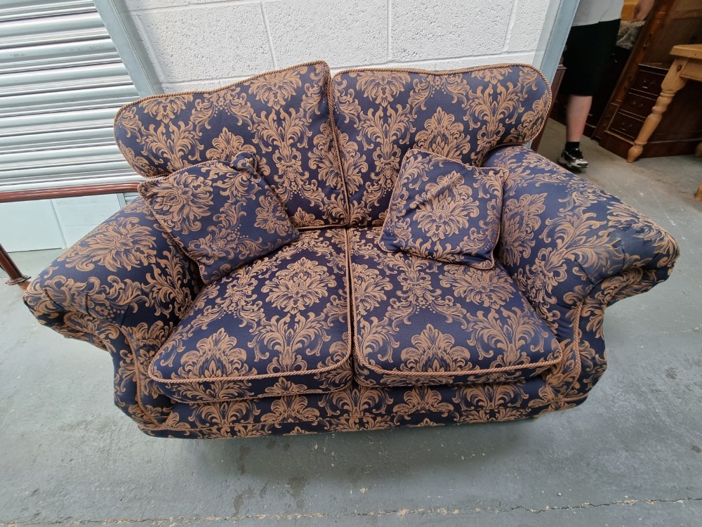 A two seater settee having scroll arms and upholstered in blue and gold fabric, loose cushions,