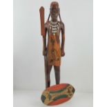 A carved wooden figurine of a tribesman with spear and shield standing 59cm high.