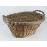 A wicker log basket of oval form having twin handles, measuring 59cm wide.