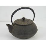 An oriental cast iron teapot having raised floral decoration upon, swing handle, oriental marks to