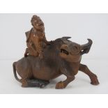 A finely carved and detailed wooden recumbent water buffalo with seated figure upon, slightly a/f,