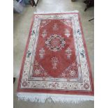 A terracotta ground woollen rug having Oriental style foliate pattern in green, purple and cream,