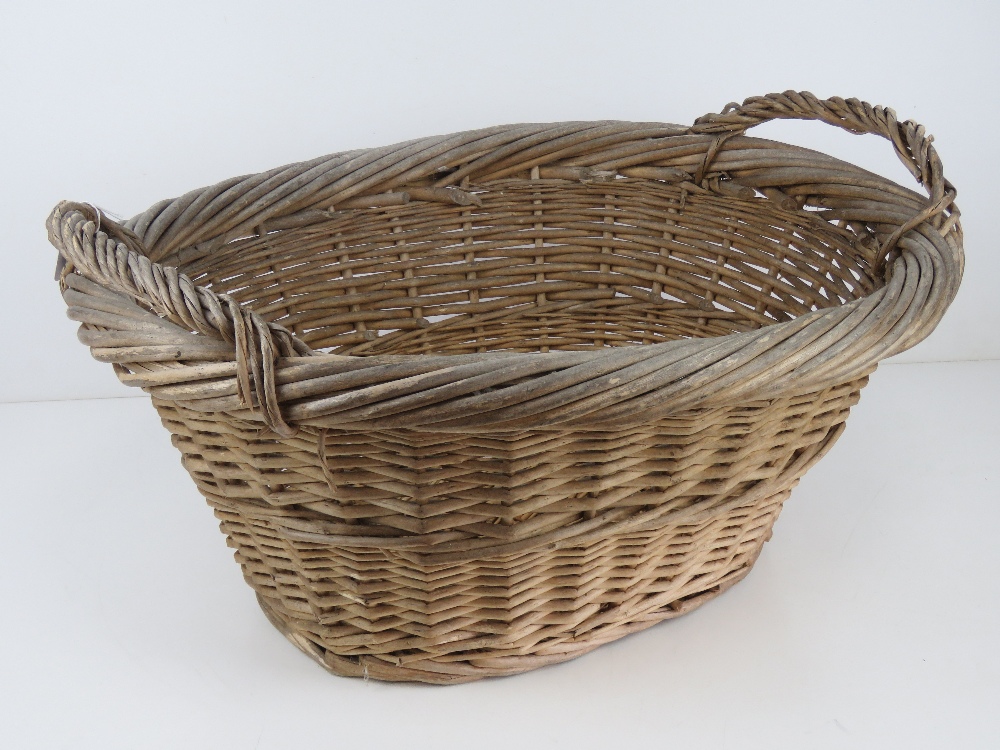 A wicker log basket of oval form having twin handles, measuring 59cm wide.