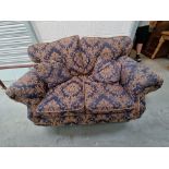 A two seater settee having scroll arms and upholstered in blue and gold fabric, loose cushions,