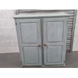 A painted pine cupboard having twin doors opening to reveal straight cut shelves within,