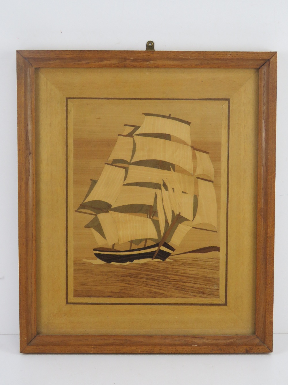 A large marquetry picture of a masted ship with sails on the sea, framed and glazed,