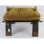 A c1970s camel saddle stool having brass fittings and golden velvet cushion.