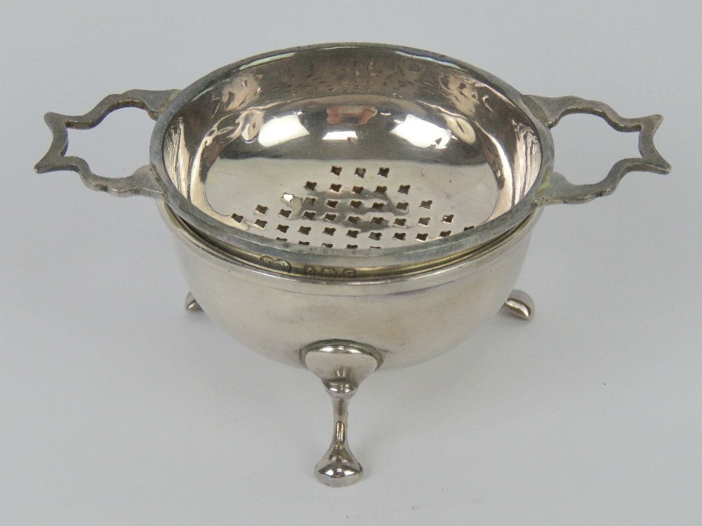 An HM silver tea strainer and bowl raised over three feet, hallmarked Birmingham 1931, 47.1g / 1.