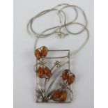A large silver and Baltic amber pendant featuring two dragonflies over a plant, with chain necklace,