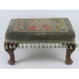 A footstool upholstered in tapestry fabric and raised over cabriole legs.
