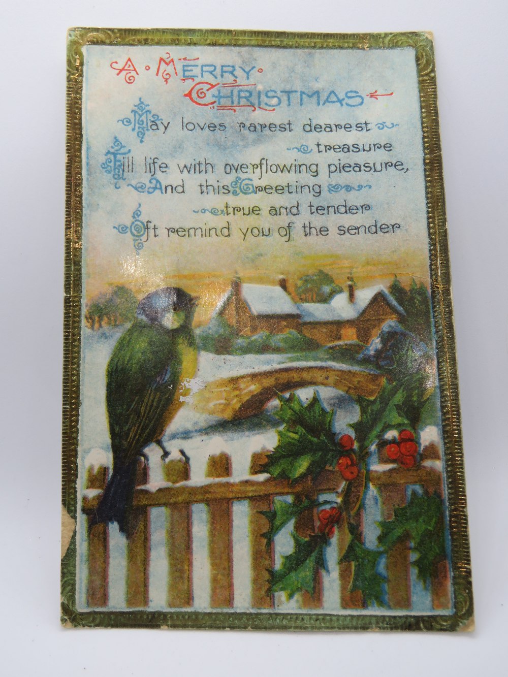 A vintage Christmas postcard featuring bird upon fence with snow covered bridge and building