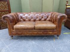 A TAN LEATHER UPHOLSTERED BUTTON BACK CHESTERFIELD SETTEE ON TURNED FEET WITH BRASS CASTORS. W 180 X