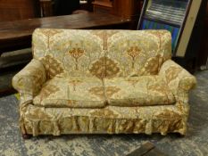 A TWO SEAT SETTEE UPHOLSTERED IN CREAM GROUND WILLIAM MORRIS STYLE FLORAL MATERIAL AND ON BUN FEET