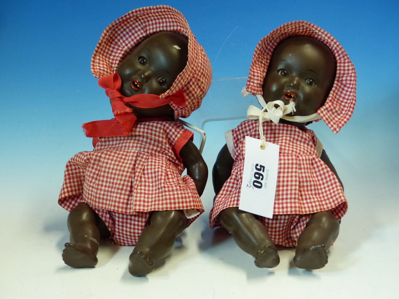 TWO SIMILAR ARMAND MARSEILLE BLACK DOLLS IN RED GINGHAM DRESSES AND BONNETS. H 27cms.