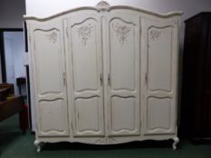 A CREAMED PAINTED WARDROBE, EACH TOP OF THE FOUR TWO PANELLED DOORS CARVED WITH SHELLS AND