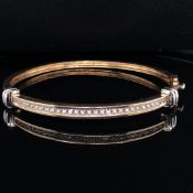 A 9ct YELLOW AND WHITE GOLD CUBIC ZIRCONIA CHANNEL SET HINGED BANGLE COMPLETE WITH TWO FIGURE OF