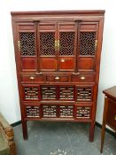 A CHINESE STAINED WOOD CABINET, THE UPPER PANELS OF THE FOUR DOORS GEOMETRICALLY PIERCED ABOVE THREE