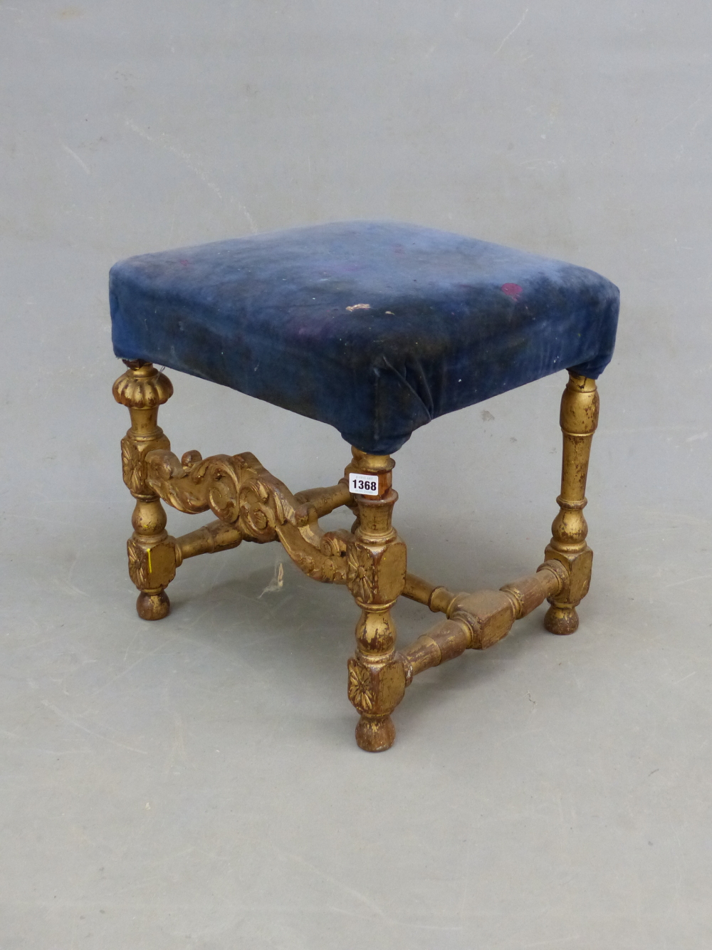 A PARCEL GILT OAK STOOL, WITH BLUE VELVET SEAT ABOVE BALUSTER LEGS JOINED AT THE FRONT BY A