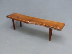 A REYNOLDS OF LUDLOW YEW WOOD BENCH, THE SEAT A SECTION OF TRUNK SUPPORTED ON FOUR CYLINDRICAL LEGS,