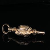 AN ANTIQUE DOUBLE SIDED GILDED POCKET WATCH KEY IN AN ORNATE CARVED SHIELD WITH A SHAPED SWIVEL