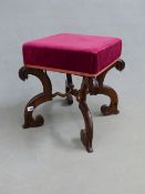 A VICTORIAN ROSEWOOD STOOL UPHOLSTERED IN RED, THE BRACKET SHAPED LEGS JOINED BY SPIRAL TURNED