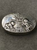 A CONTINENTAL SILVER OVAL FORM PILL BOX DEPICTING CHERUBS IN A GARDEN SCENE. MEASUREMENTS 4.7cms x