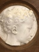 AN OAK FRAMED WHITE MARBLE RELIEF ROUNDEL DEPICTING A YOUNG PERSONS HEAD, THE MARBLE. Dia. 25cms.