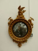 A REGENCY CONVEX MIRROR, THE GILT CIRCULAR BEADED FRAME SURMOUNTED BY THREE DOLPHINS, A PENDANT OF