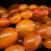 A GRADUATED ROW OF OVAL CYLINDRICAL AMBER BEADS, WITH A GOLD PLATED SCREW DOWN CLASP. GROSS WEIGHT