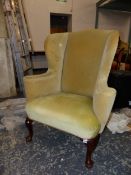 A GEORGE III STYLE WING BACKED ARMCHAIR, THE MAHOGANY LEGS ON PAD FEET