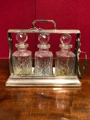 A THREE BOTTLE ELECTROPLATE TANTALUS, THE SPIRIT DECANTERS WITH FACETTED STOPPERS, THE