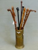 A BRASS CYLINDRICAL STAND OF ELEVEN WALKING CANES AND STICKS, TO INCLUDE: AN EBONISED CANE WITH