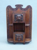 AN UNUSUAL CARVED OAK ARTS AND CRAFTS CABINET WITH SIDE SHELVES. LION MASK DROP FRONT