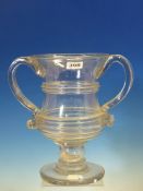 A TWO HANDLED CLEAR GLASS CUP, THE WAISTED CYLINDRICAL BOWL APPLIED WITH HORIZONTAL RIBBED BANDS,