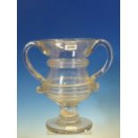 A TWO HANDLED CLEAR GLASS CUP, THE WAISTED CYLINDRICAL BOWL APPLIED WITH HORIZONTAL RIBBED BANDS,