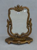 A DRESSING TABLE MIRROR, THE SHAPED PLATE WITHIN GILT ROCOCO FOLIAGE FRAME CRESTED BY A WINGED