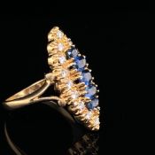 AN 18CT YELLOW GOLD SAPPHIRE AND DIAMOND NAVETTE RING. A ROW OF FIVE GRADUATED OVAL SAPPHIRES RUN